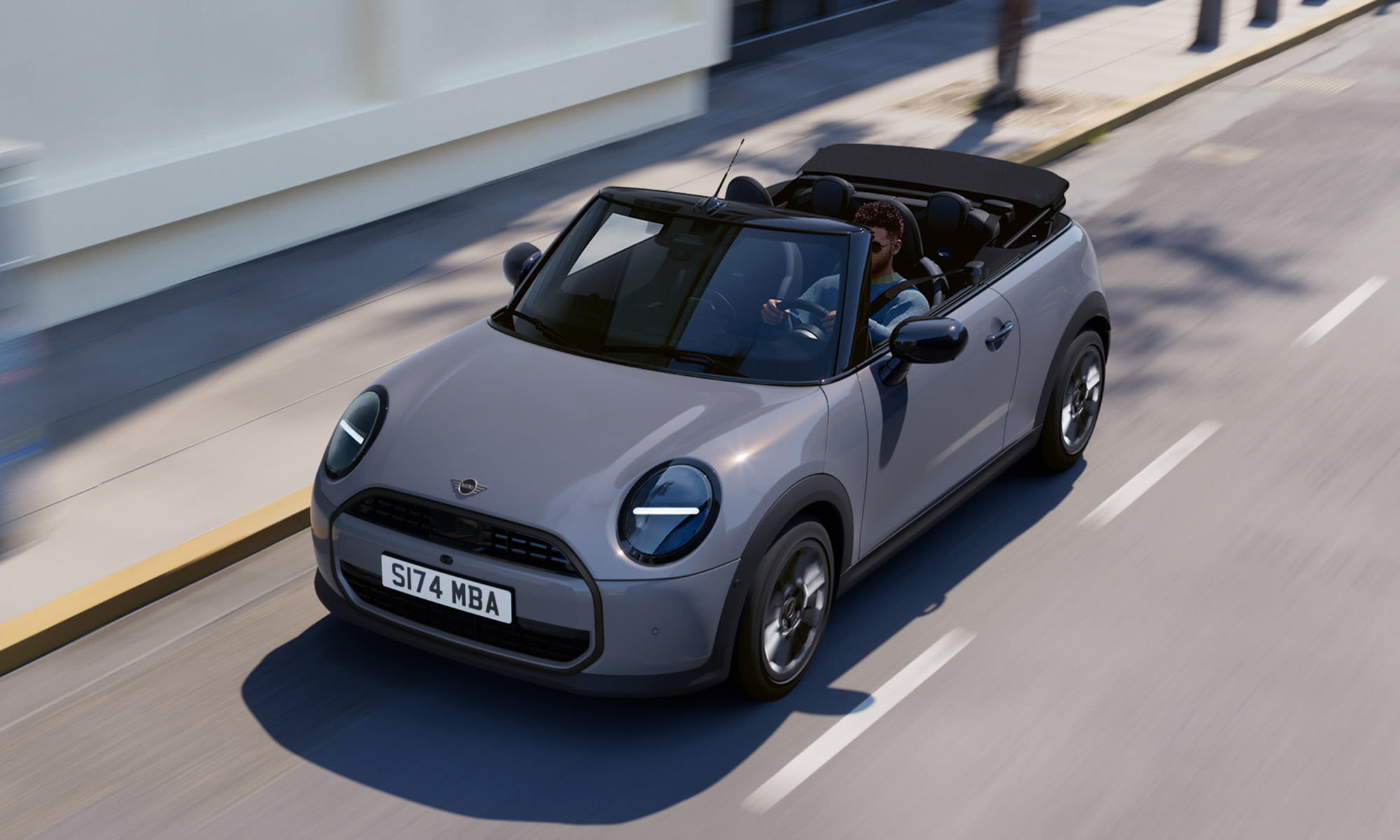 Grey MINI Convertible driving along a city street with the roof down.
