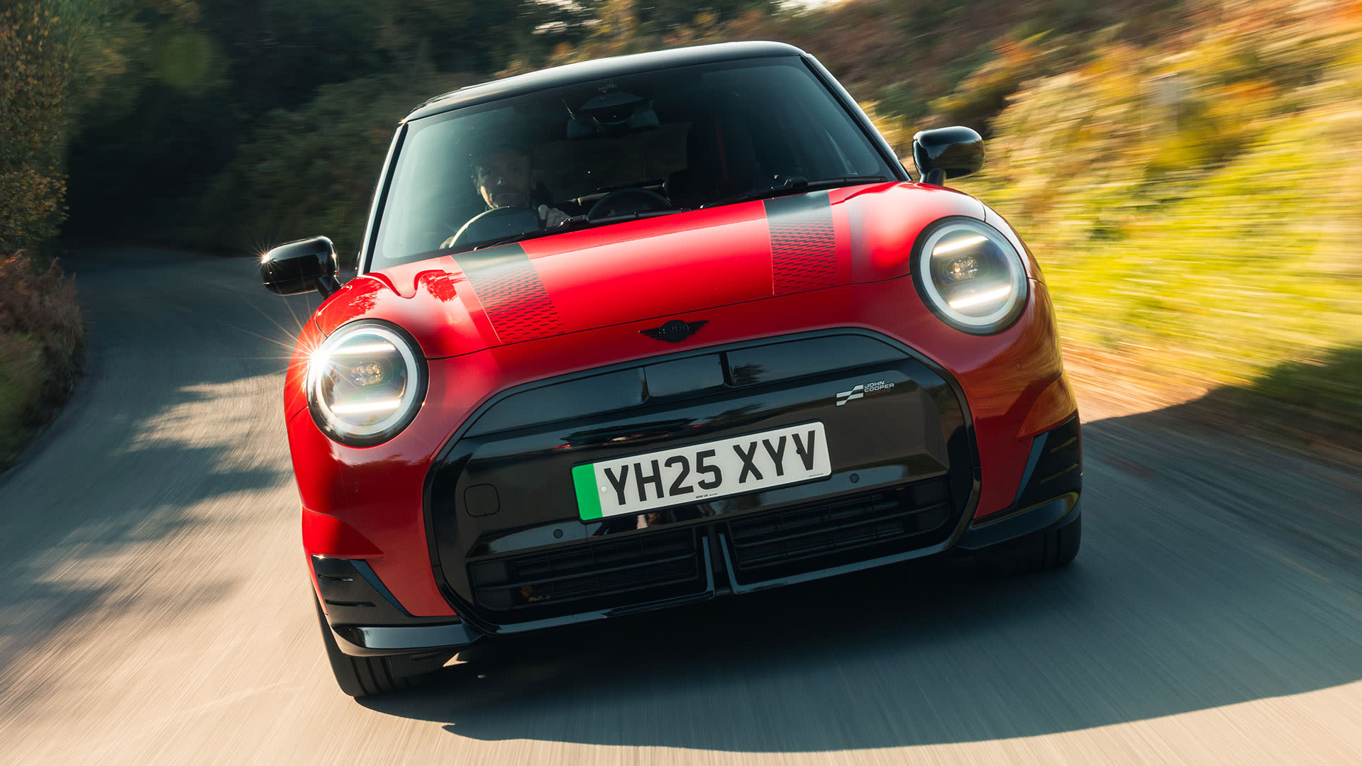 Front view of a red MINI driving along a tree‑lined rural road.