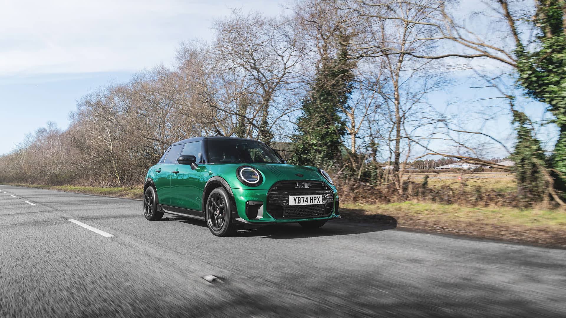 Green MINI driving along a tree‑lined rural road.