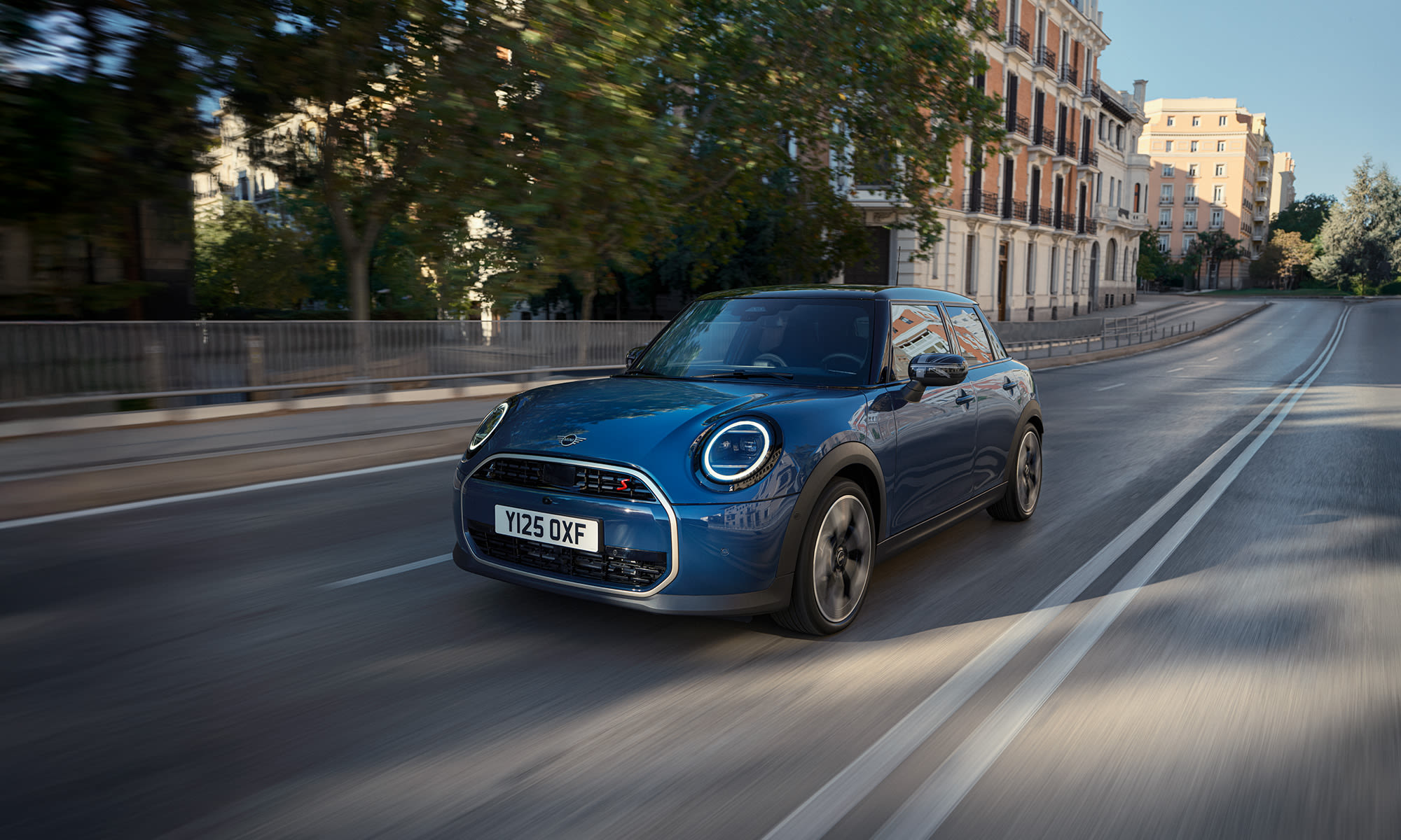 Blue MINI Cooper driving along a city street with motion blur.