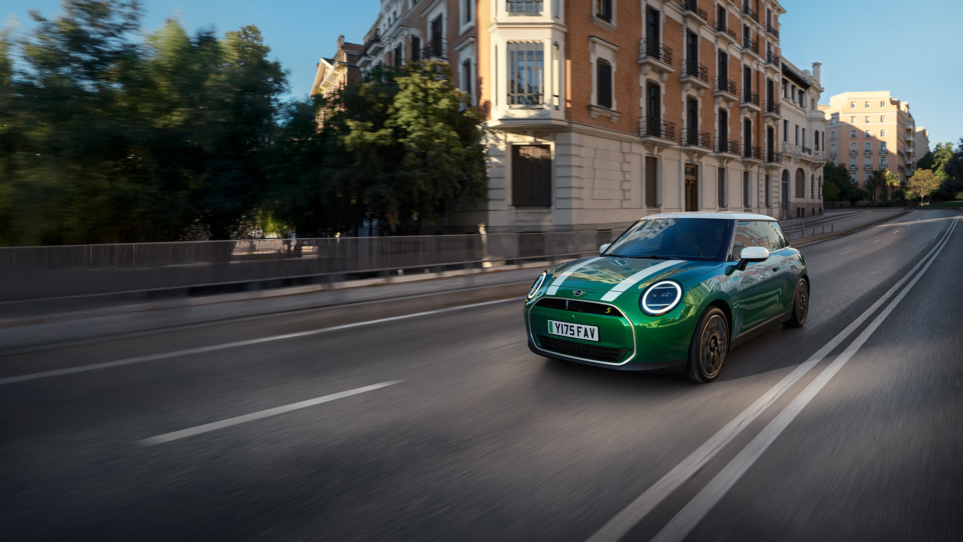 Green MINI Cooper Electric on a city road with building in the background.