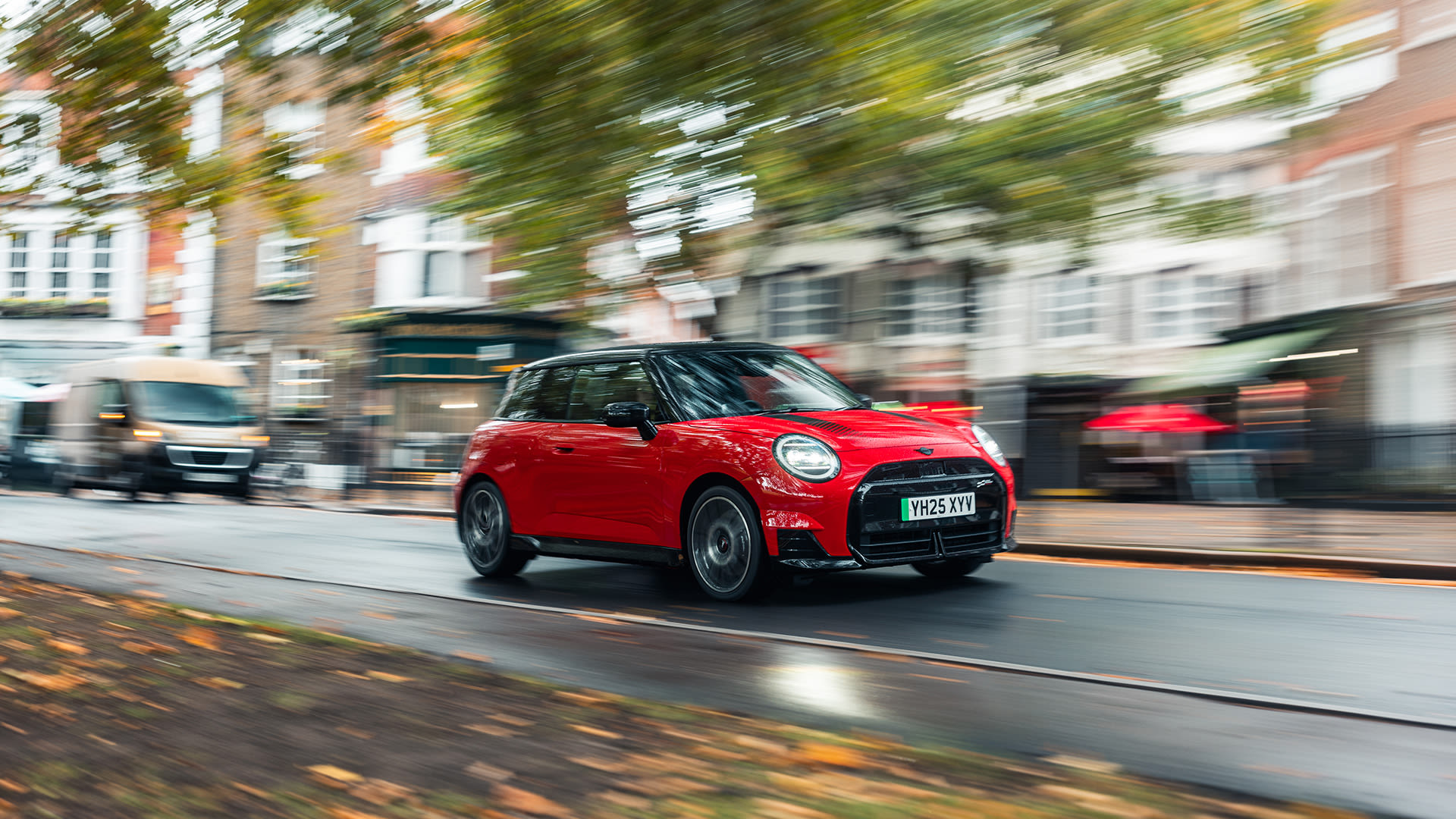 Red MINI Cooper 3 door driving on a street with buildings on the right side