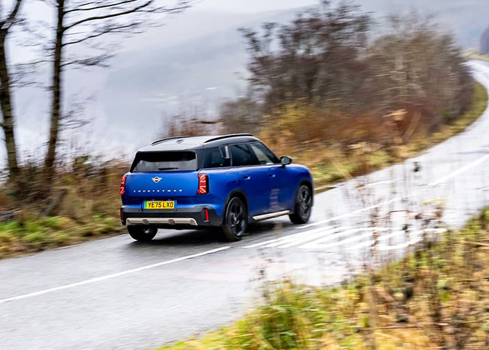 Rear view of a blue MINI Countryman Electric driving on a wet country road.
