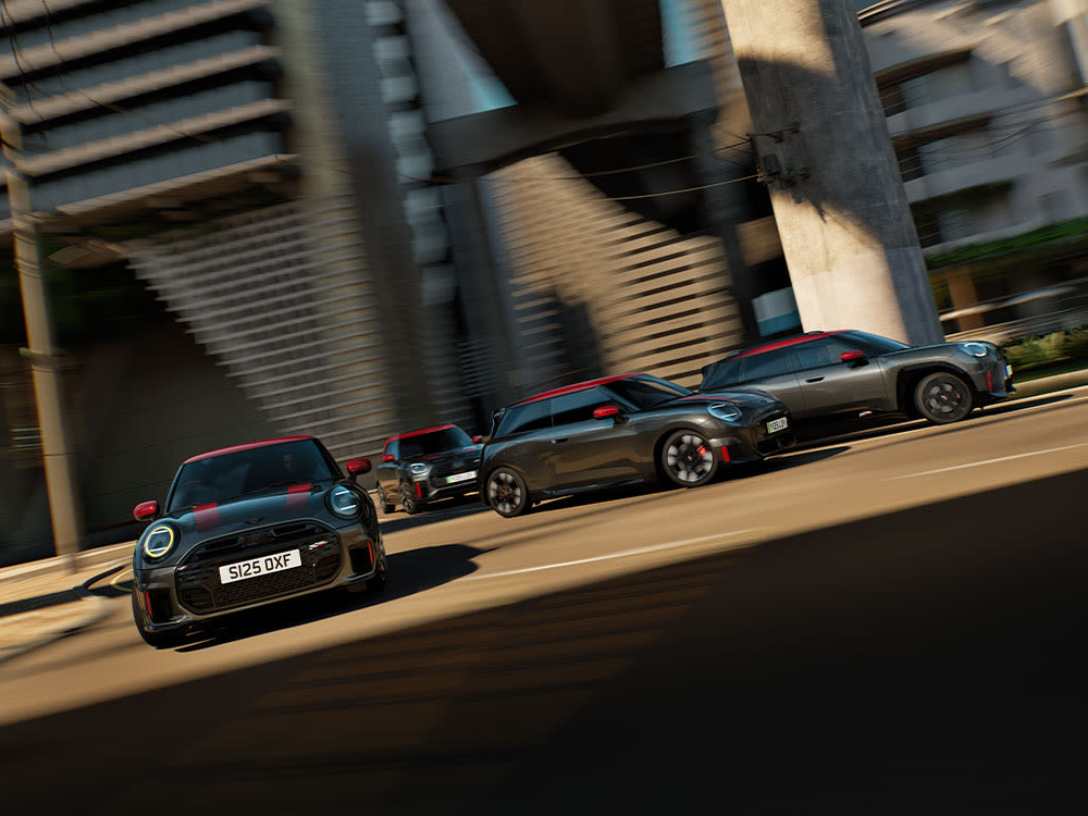 Five MINI John Cooper Works cars with red roofs parked in a row in an urban setting with buildings and a construction site in the background.