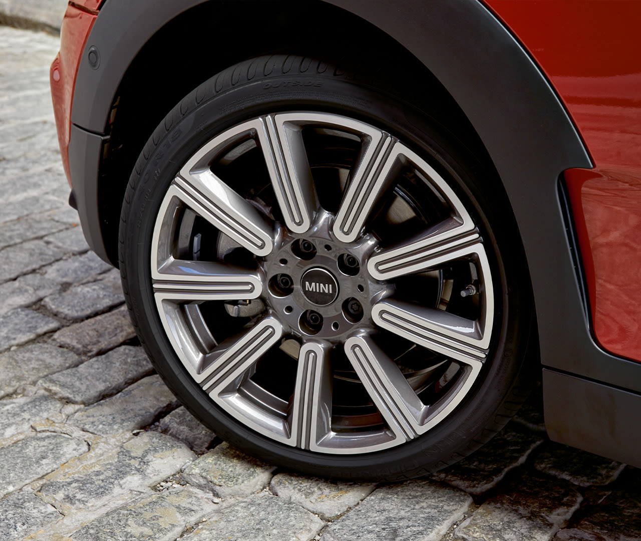 Close-up of a MINI's front wheel with floating hub caps, parked on a cobblestone street.