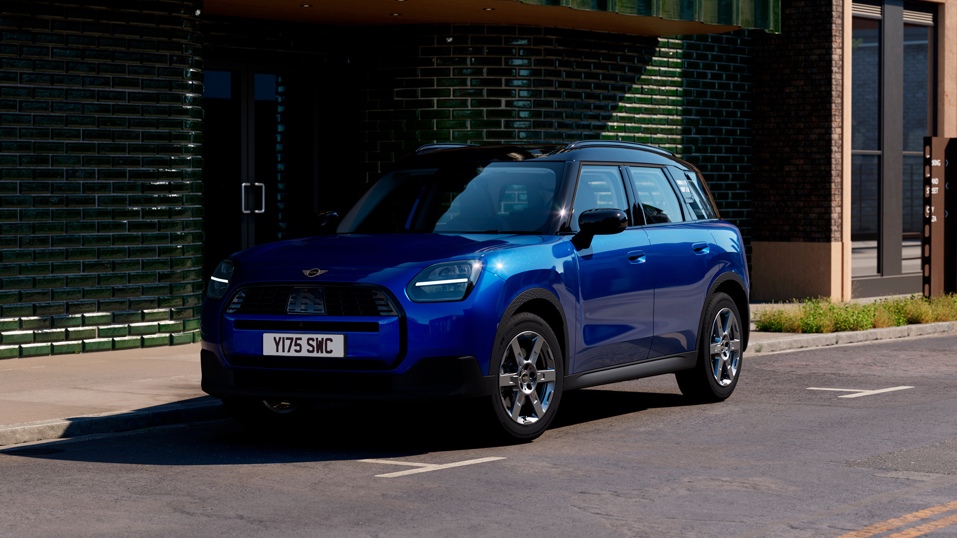 A blue MINI Countryman parked on the side of a street in front of a modern building with green and brick walls.