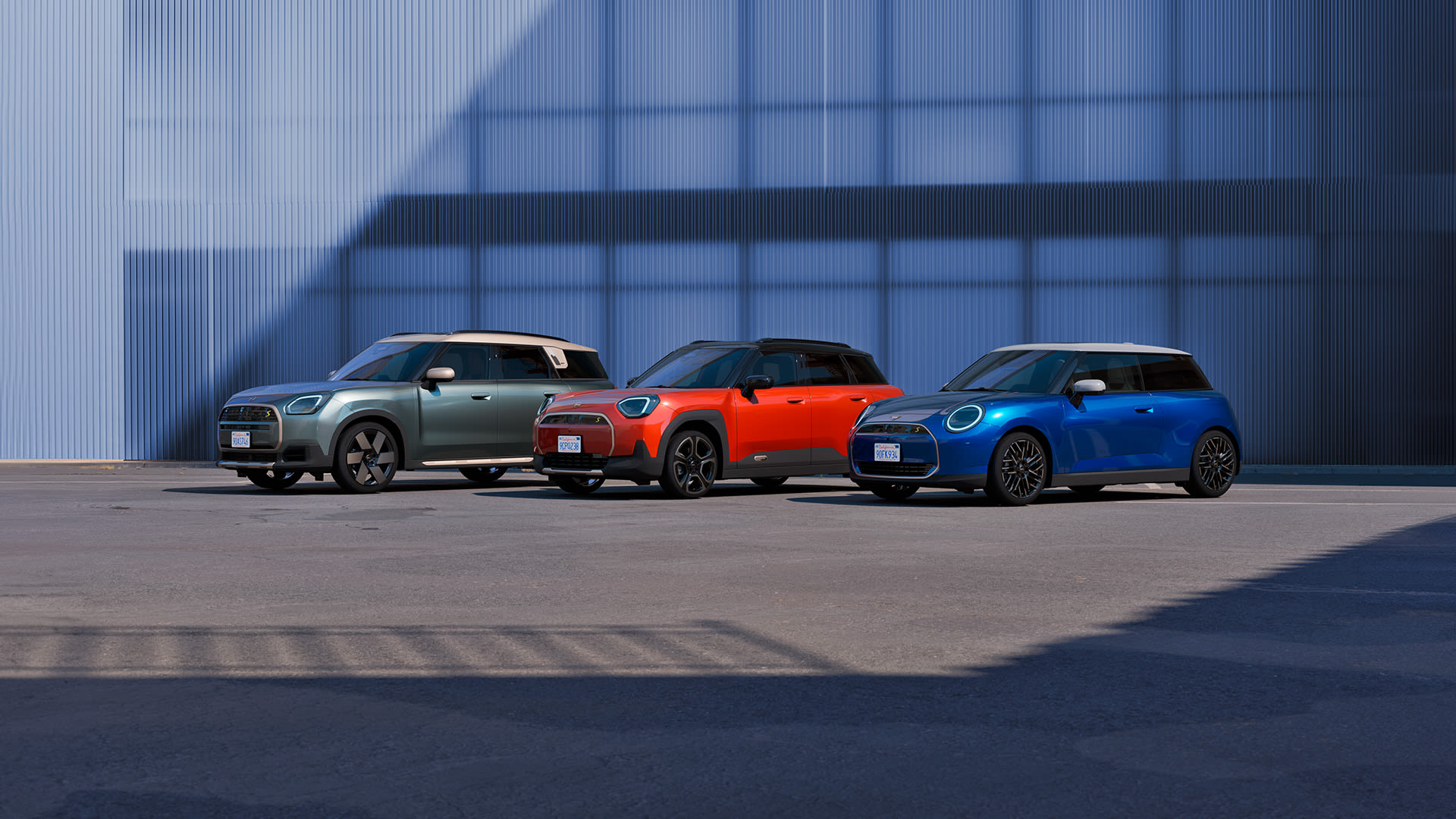 Green, orange, and blue MINI models parked outdoors against a modern blue wall.