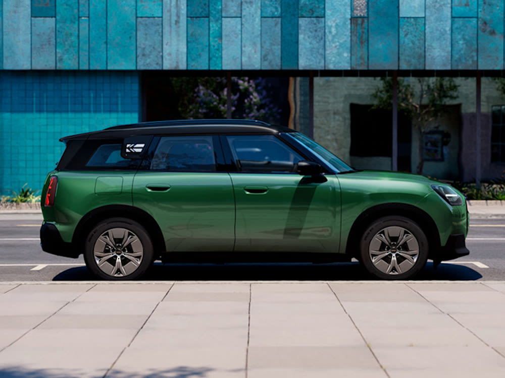 Side view of a green MINI Countryman electric parked on a road with a blue building in the background