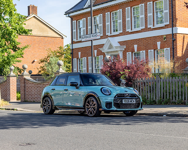 Blue MINI Clubman parked on a residential street outside red-brick houses on a bright, sunny day.