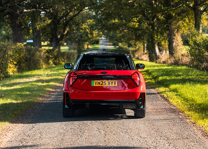 Red MINI Cooper Electric on a country road with green trees on both sides of the road.