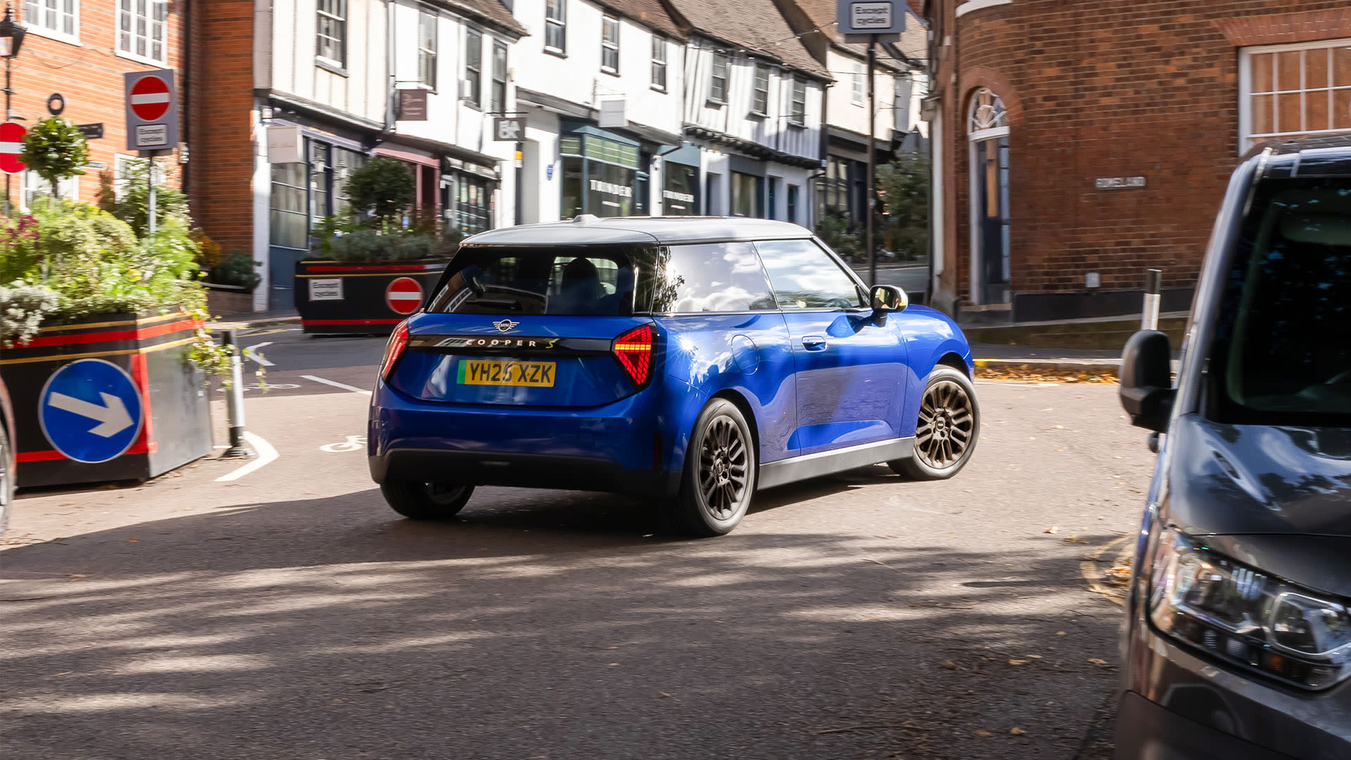 Blue MINI Cooper driving through a town street with brick buildings.