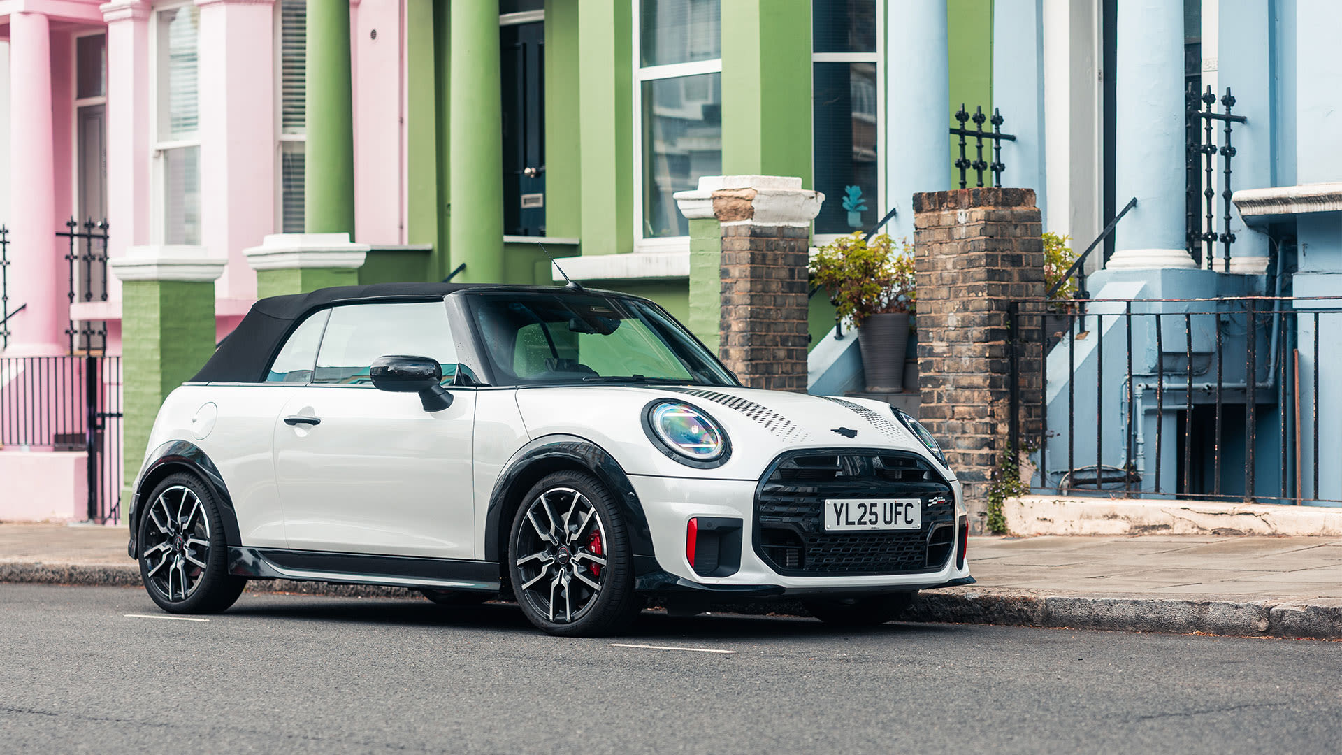 White MINI Convertible parked on a residential street with colourful terraced houses in the background.