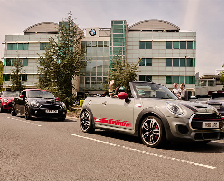 Different models of MINI in a convoy with a modern building in the background with a BMW sigil on top