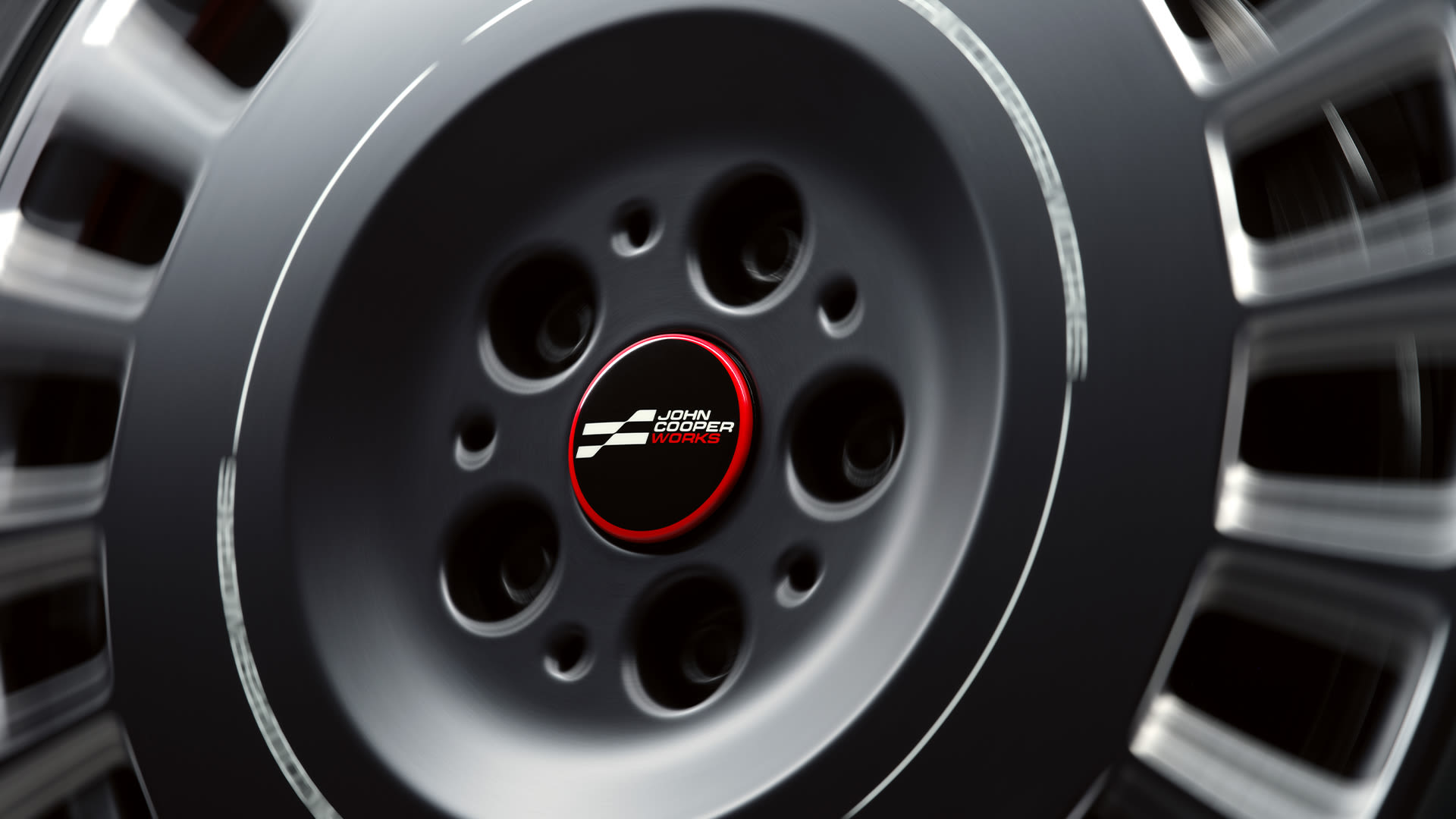 Close-up of a spinning car wheel with a black and red center cap featuring the John Cooper Works logo.