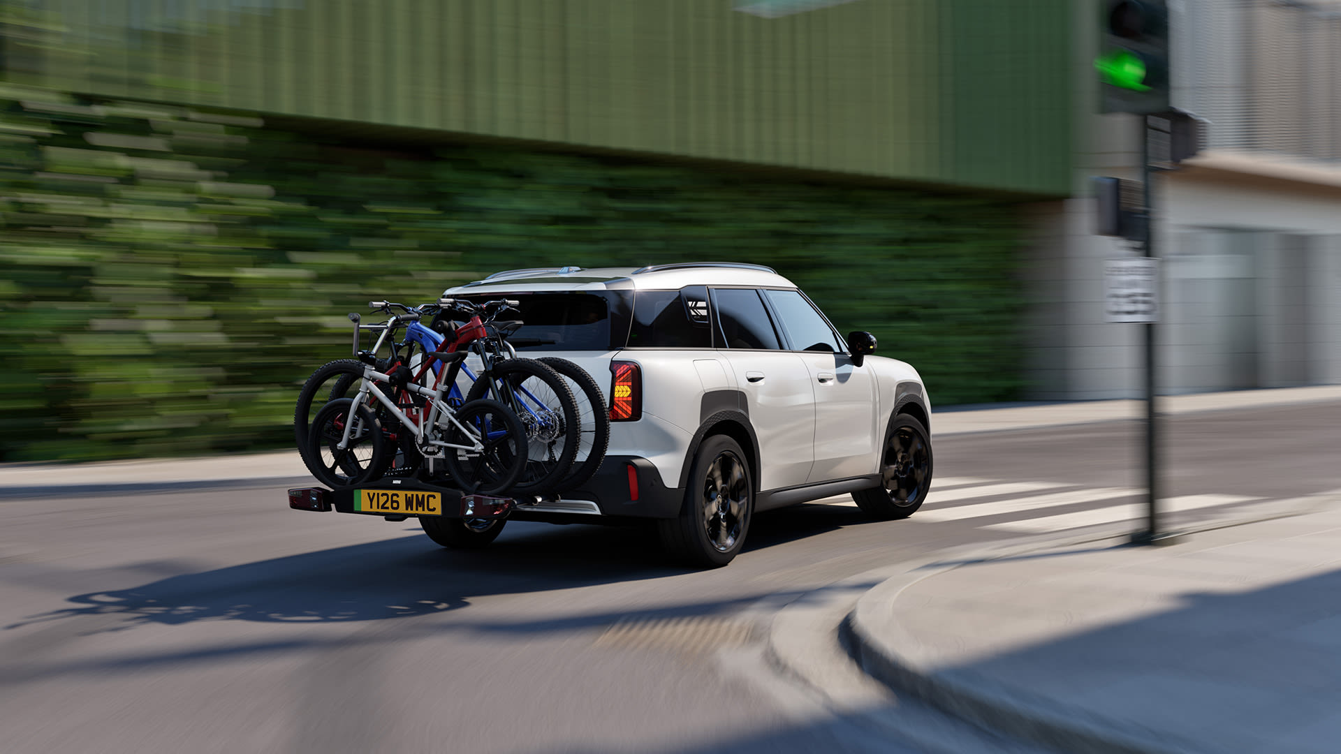 White MINI Countryman driving through a city street with two bicycles mounted on a rear rack.