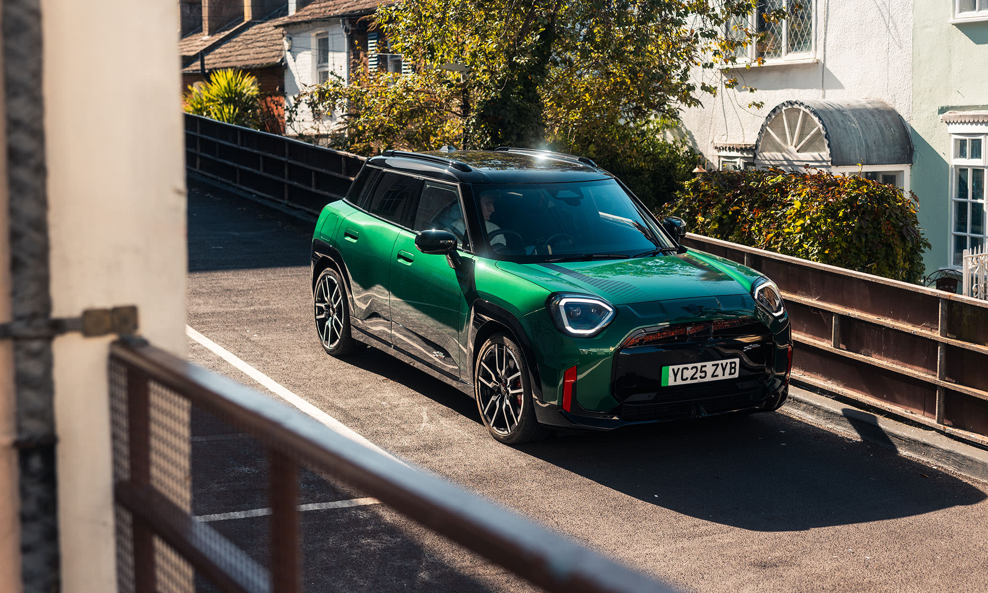 Green MINI Aceman JCW Electric driving along a residential street.