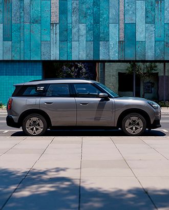 Side view of a grey MINI Countryman parked on a city street in front of a modern building.