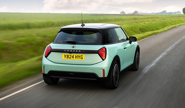 Rear three-quarter view of a mint green MINI Cooper driving along a country road.