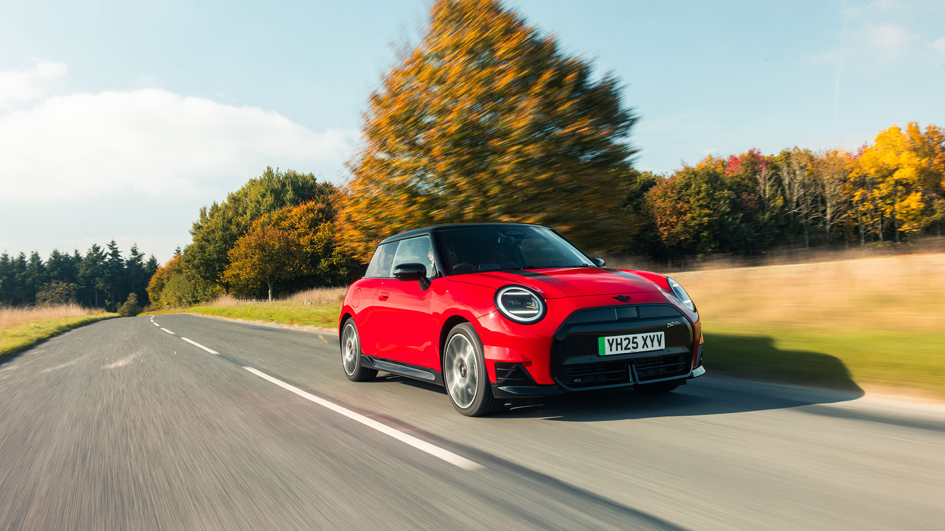 Red MINI driving along a winding country road with autumn trees.