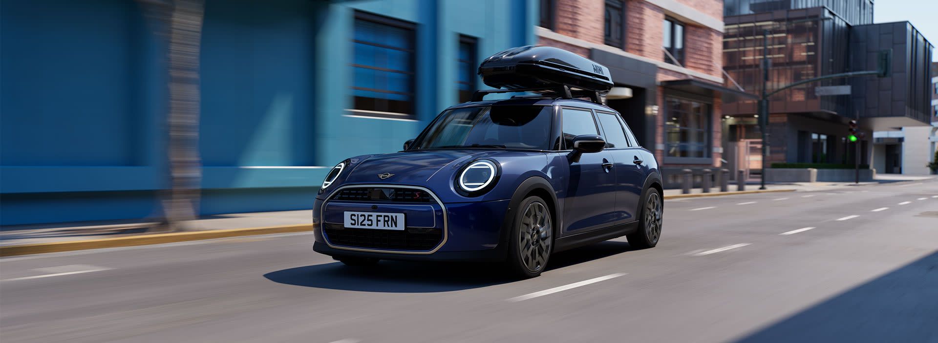 Blue MINI car driving through a city street with a roof-mounted cargo box.