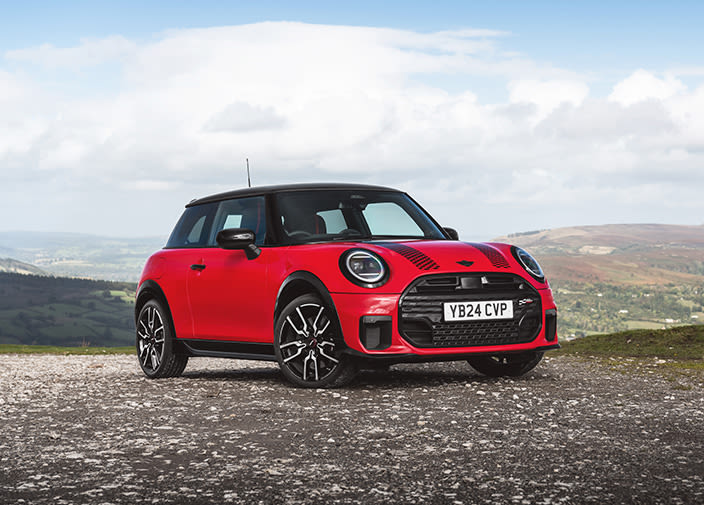Front view of a red MINI Cooper on a gravel spot with hills view in the background