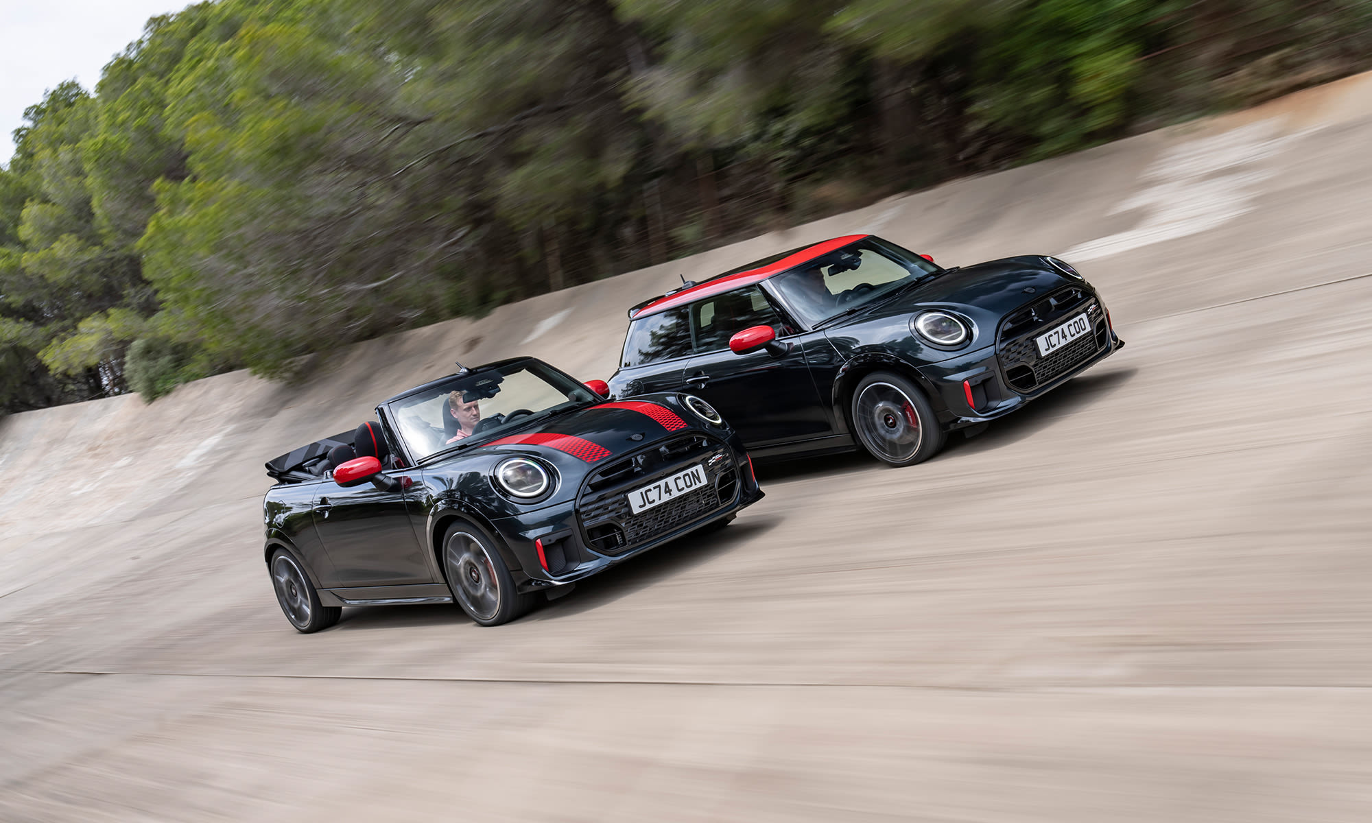 Two MINI John Cooper Works models driving side by side on a dirt track.
