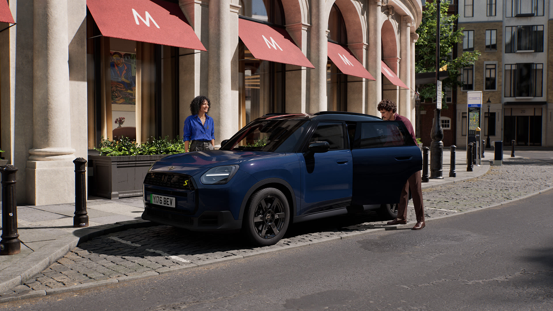 Blue MINI Aceman parked on a cobbled city street outside a building with red awnings, as occupants enter and exit.