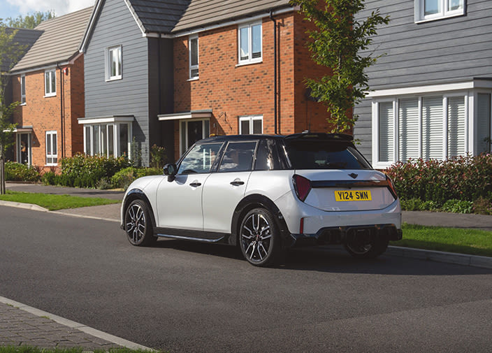 Left back view of a white 5 door MINI cooper with black roof parked on a street in front of a house