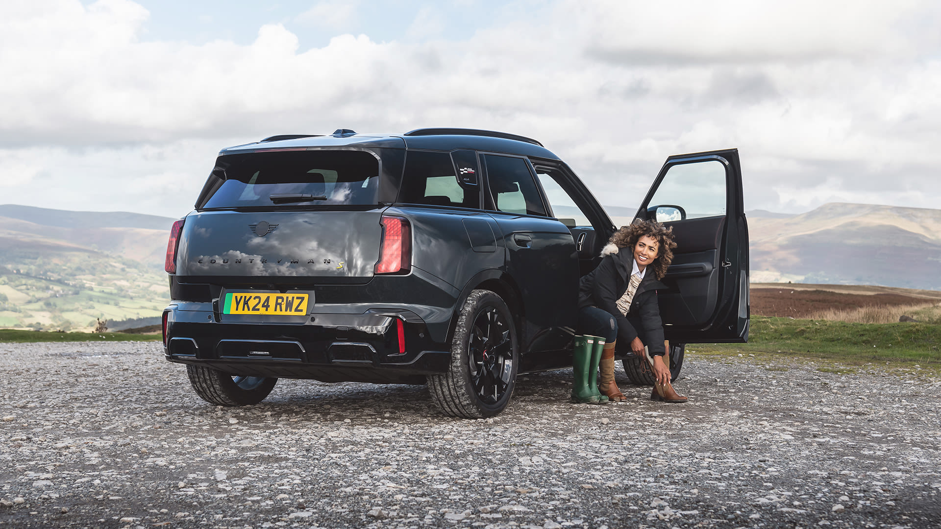 A black MINI Countryman electric parked on a gravel spot with hills and valleys in the background