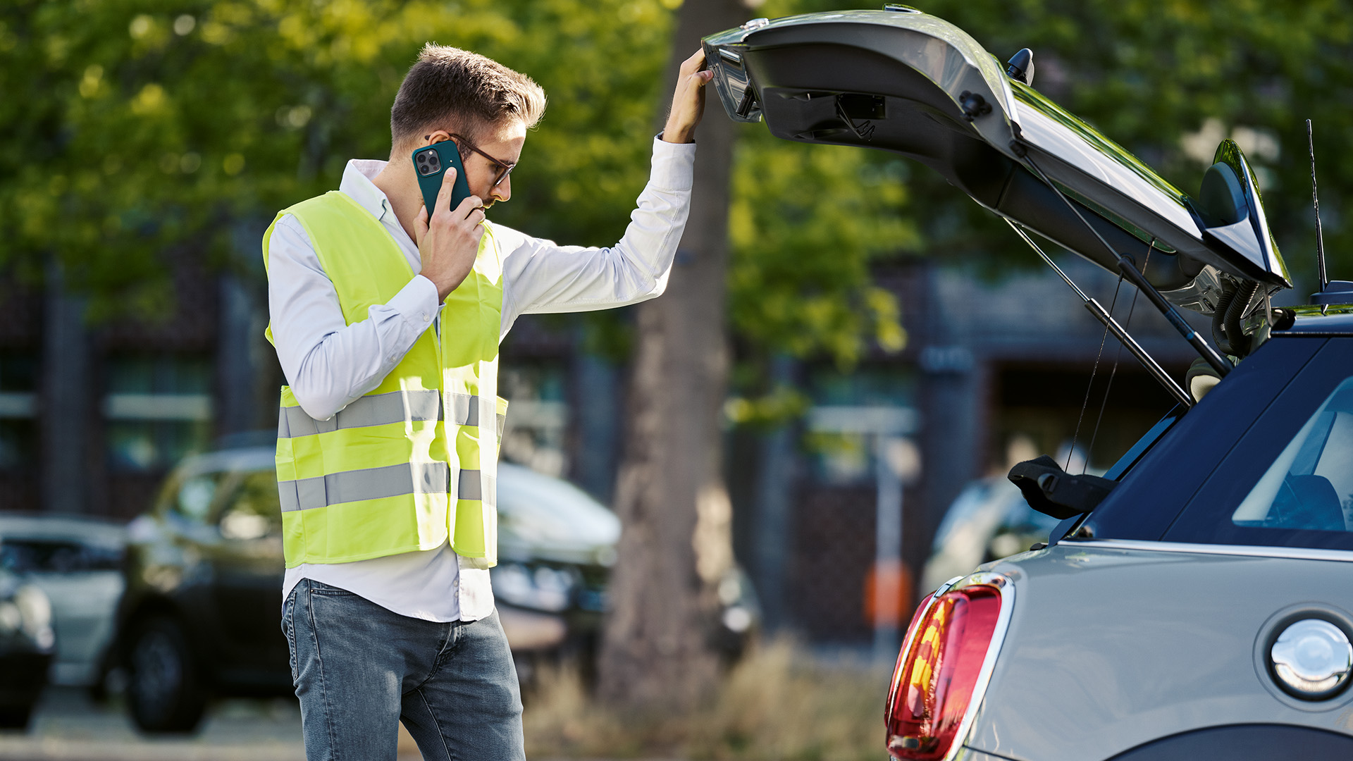 Man with yellow vest speaking on mobile phone and looking inside of a MINI car boot