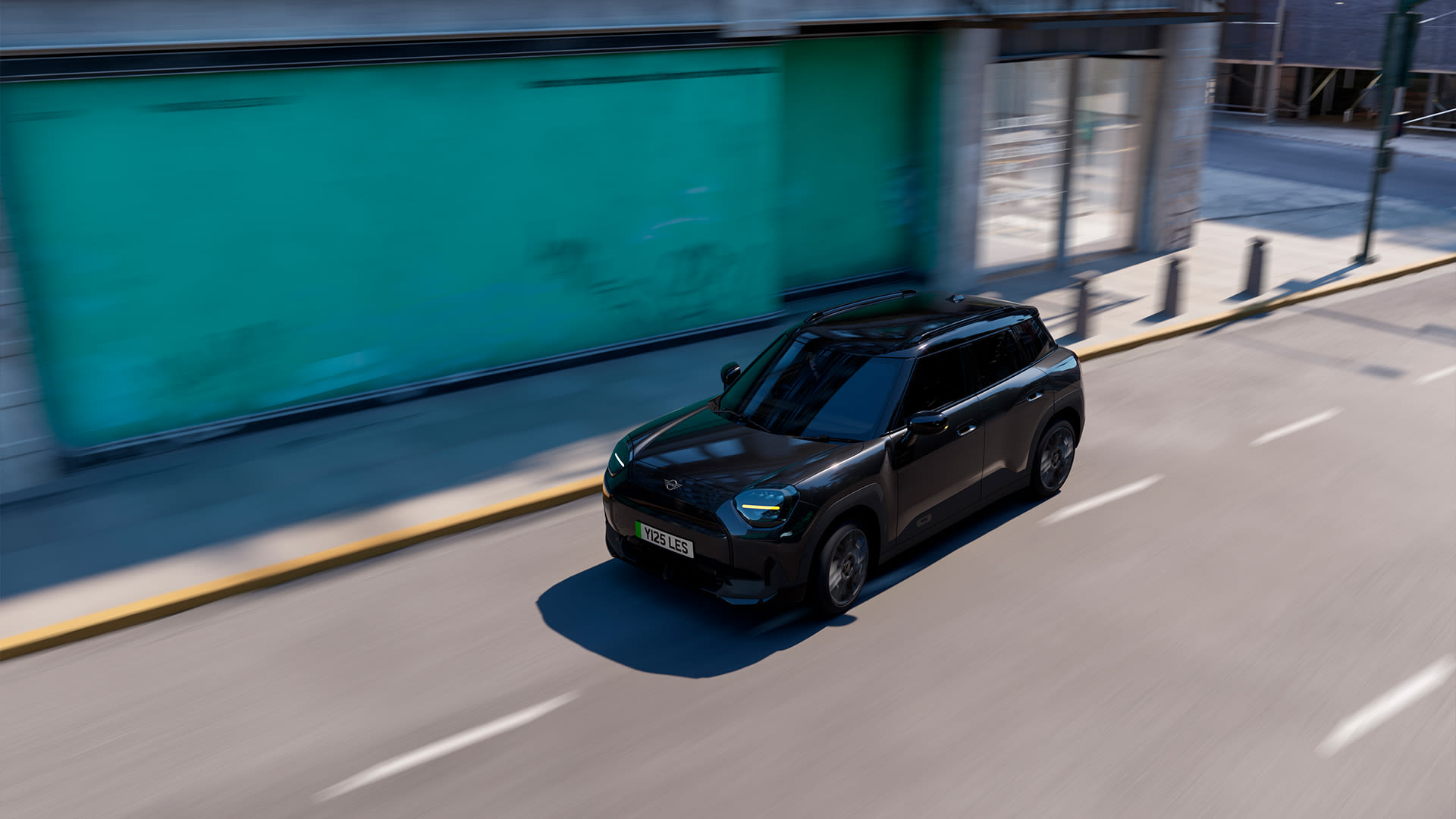 Monochrome MINI Aceman driving on a quiet urban street with a green building in the background