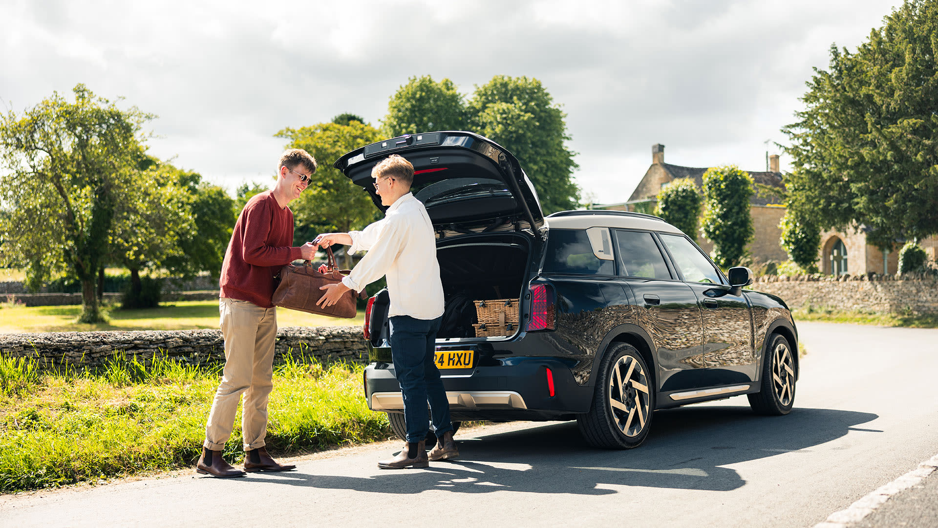 Two people loading a bag into the open boot of a black MINI Countryman parked on a rural road.