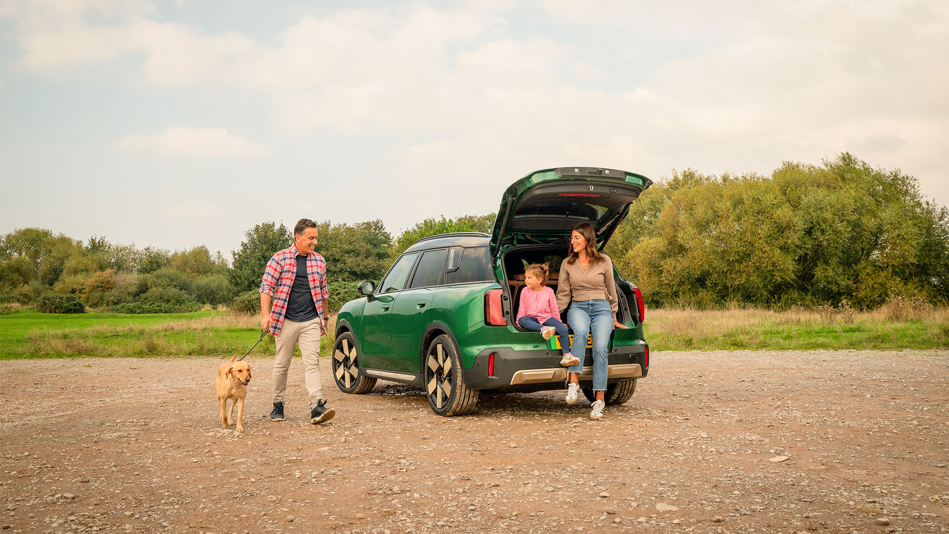 Green MINI car with open tailgate, people gathered at the rear of the vehicle in a countryside setting.