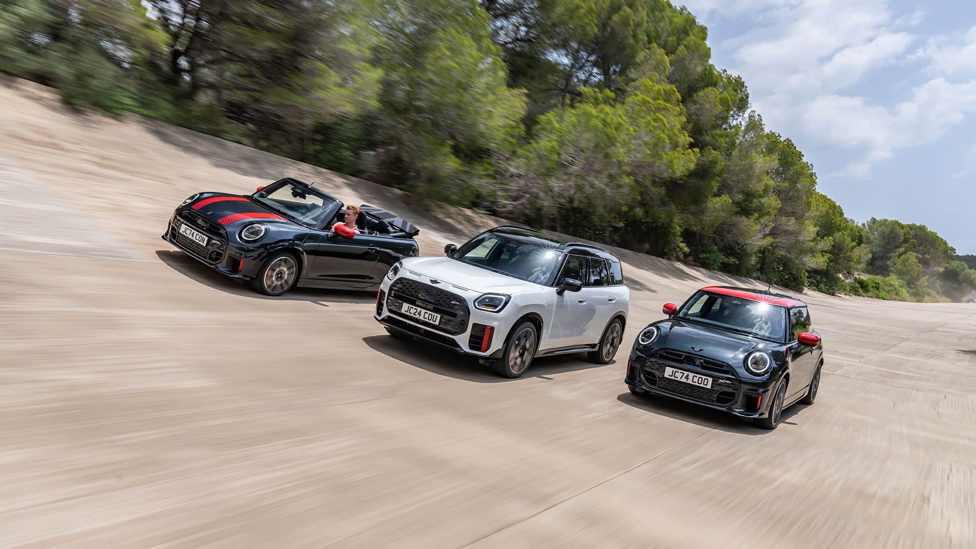 Three MINI cars driving side by side on a track, with trees in the background.