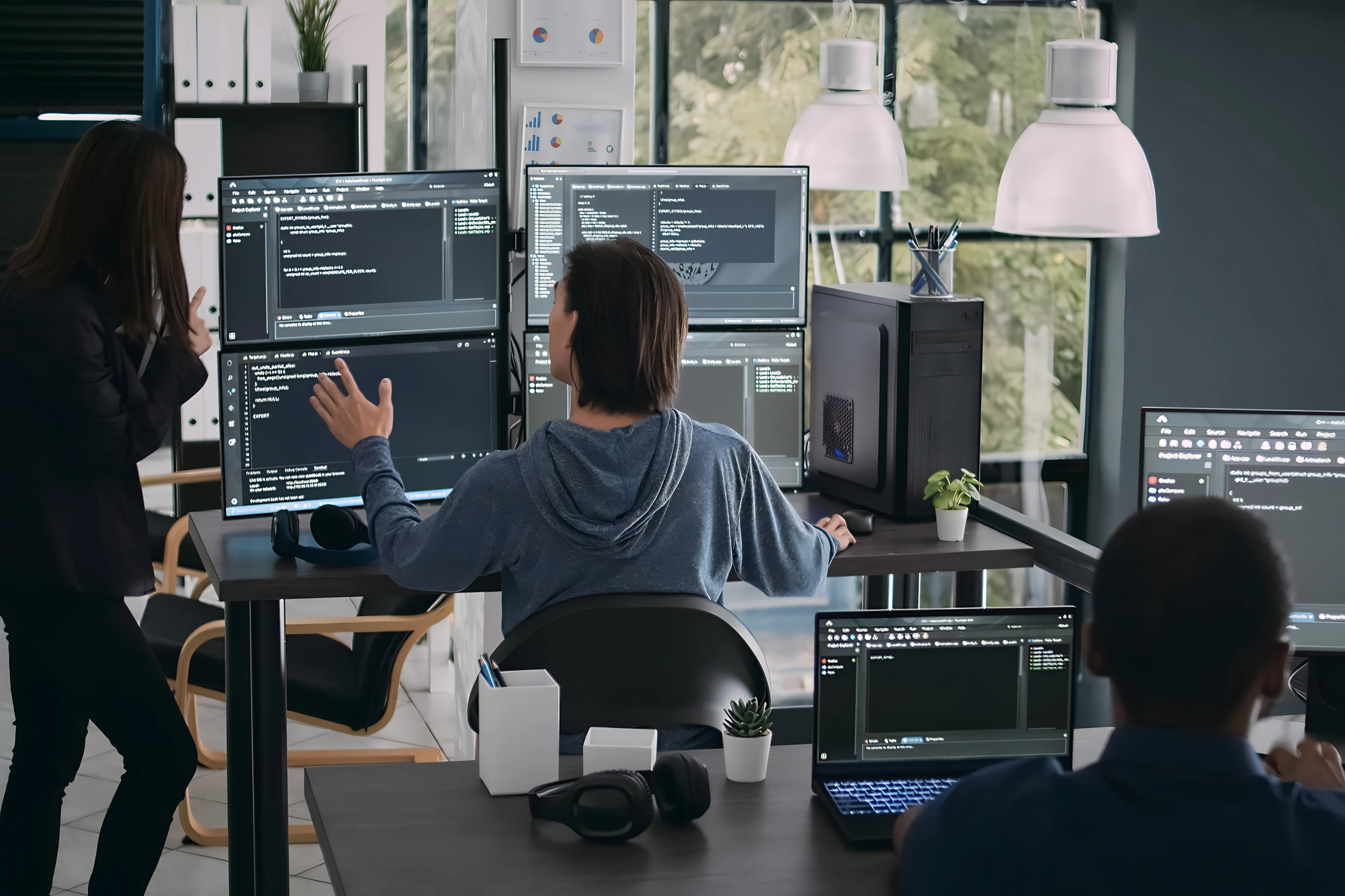 Woman standing next to a man sitting with four screens in front of him.