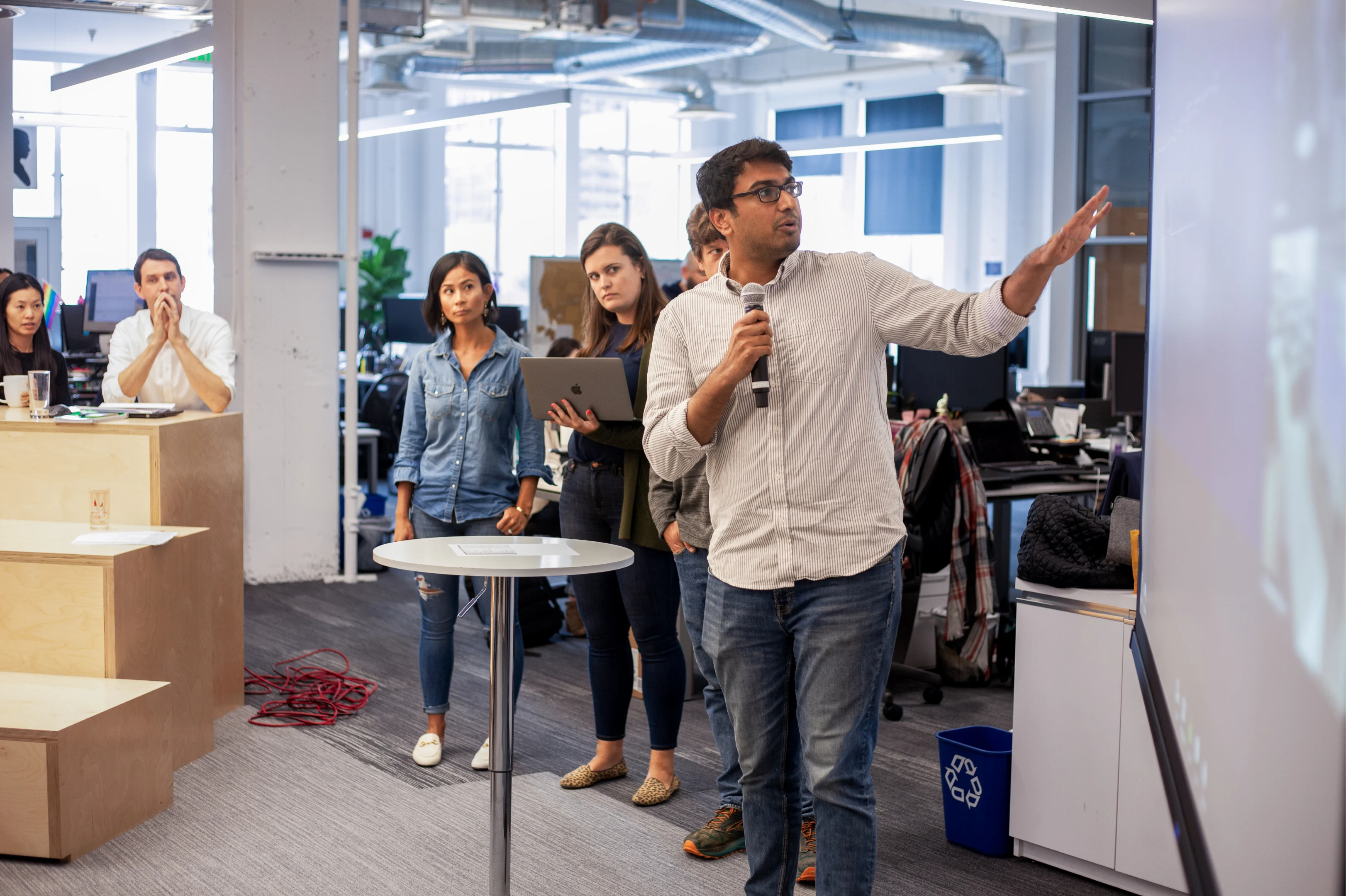 A man holding a microphone giving a presentation to a group of people in an office