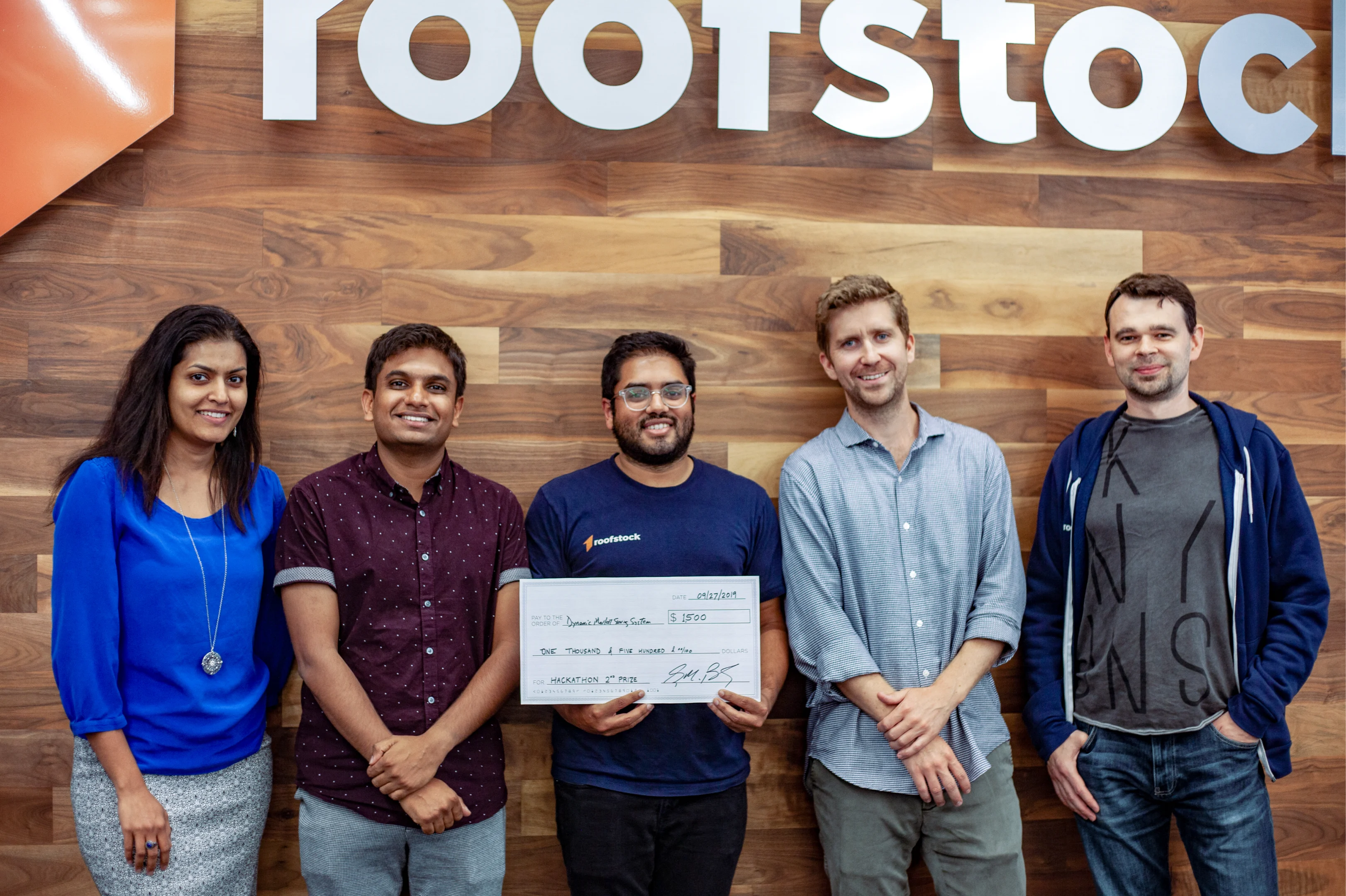 Five people standing in front of a wall holding an oversized check