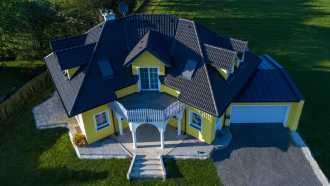 Haus mit verschiedenen Dachformen, gelber Fassade und großem Balkon als auch Garage