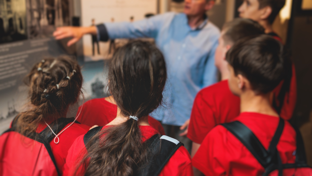 Children on a field trip in red t-shirts, watching their teacher point out and explain something interesting