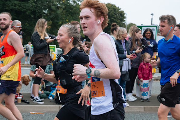 A Shelter runner running alongside other runners in the race. Behind the runners are a group of spectators. 