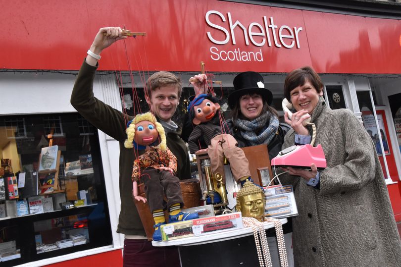 People showing some of the items available at Shelter Scotland's Stockbridge shop's annual January event. This includes two large Pelhams Puppets, a pink 1960s vintage telephone, an Ede & Ravenscroft Man’s Herringbone wool coat and a Victorian silk top hat.