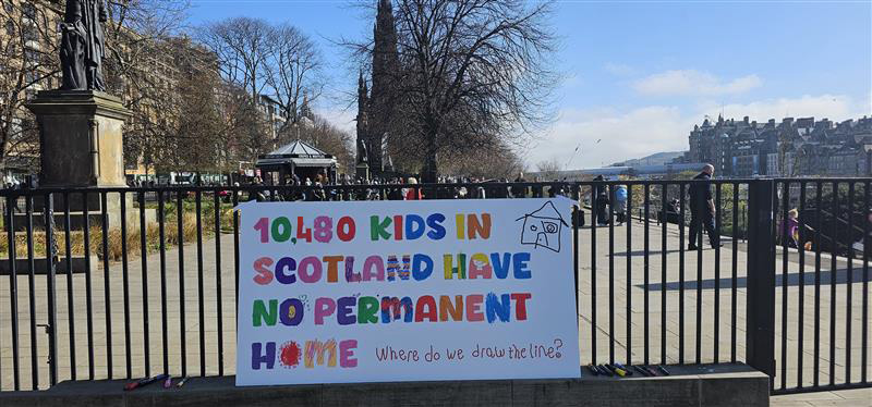 A banner attached to a railing in Princes Street Gardens in Edinburgh. The banner says that 10,480 kids in Scotland have no permanent home.