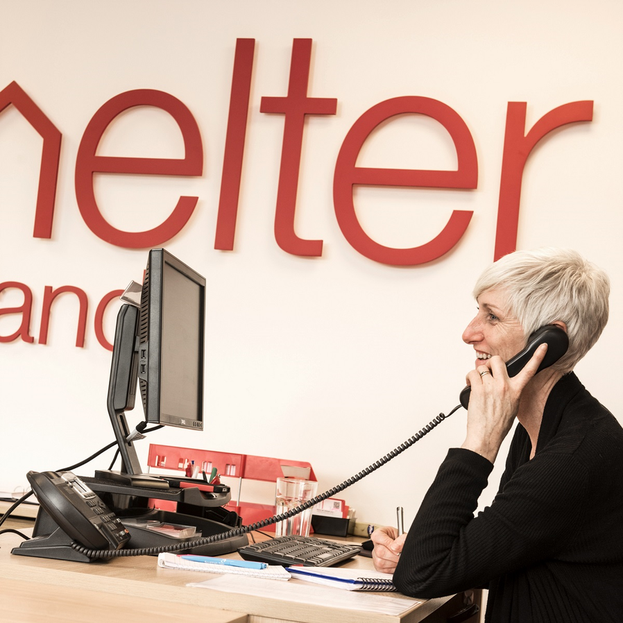 A Shelter adviser at her desk, on the phone, smiling 