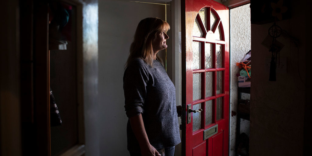 A woman standing by her open front door looking outside.