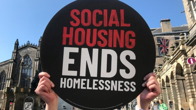 Photograph of circular sign that says social housing ends homelessness, in front of a blue sky