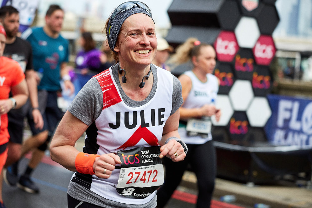 A marathon runner smiles into camera, she is wearing a running vest with a Shelter logo (photo by Matt Pull at London Marathon 2023)