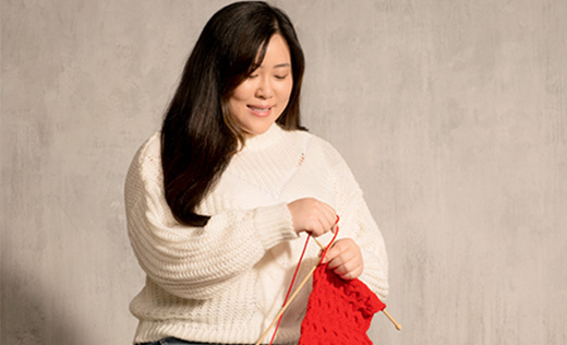A young woman knitting a red scarf and smiling