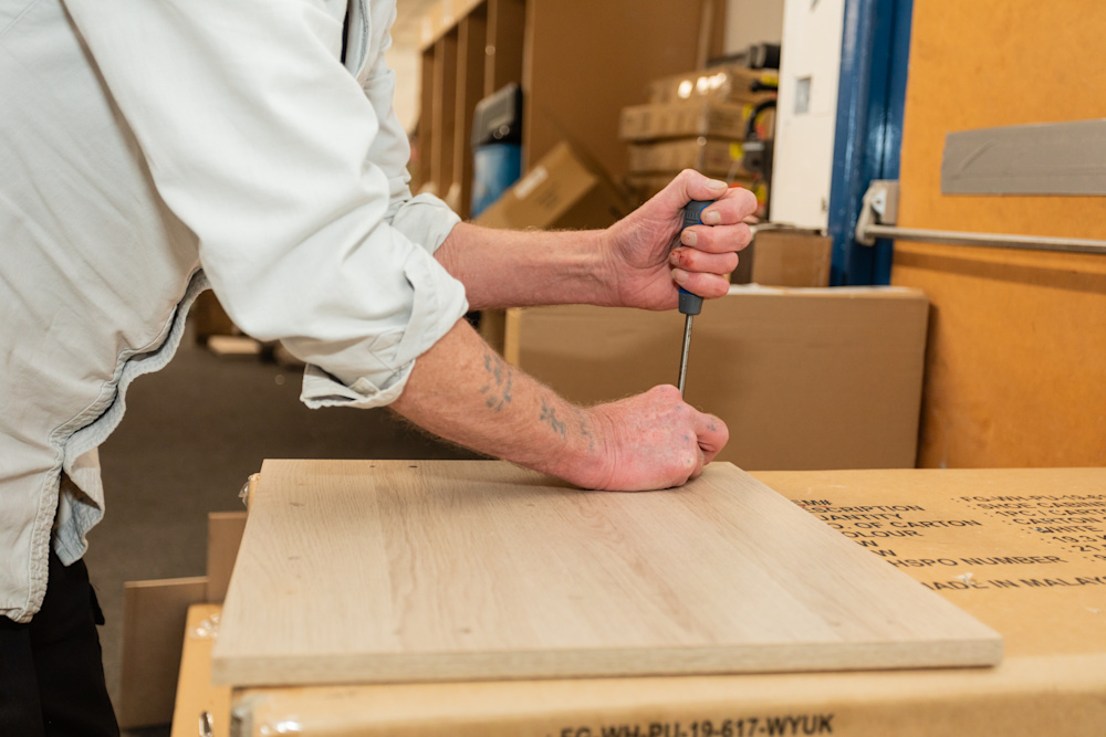 A close-up of a wooden furniture part, which a volunteer is working on with a screwdriver.