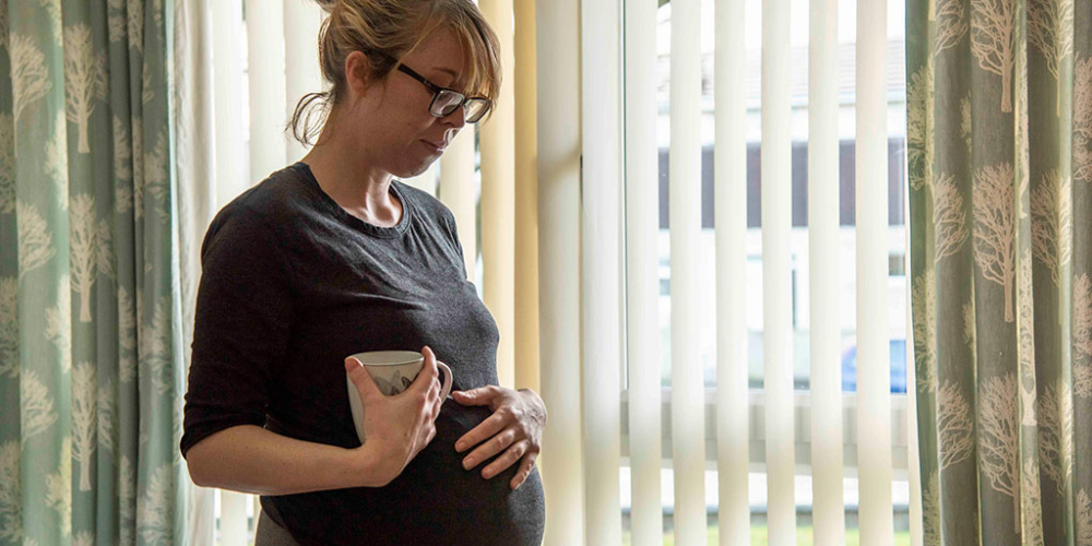 Stephanie is pregnant and pictured holding a mug with her other hand placed on her belly. 