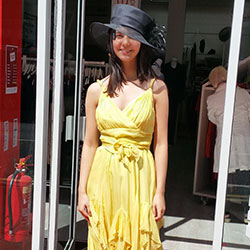 A woman wearing a yellow dress with a formal black hat outside the Byre Road Shelter Scotland shop.